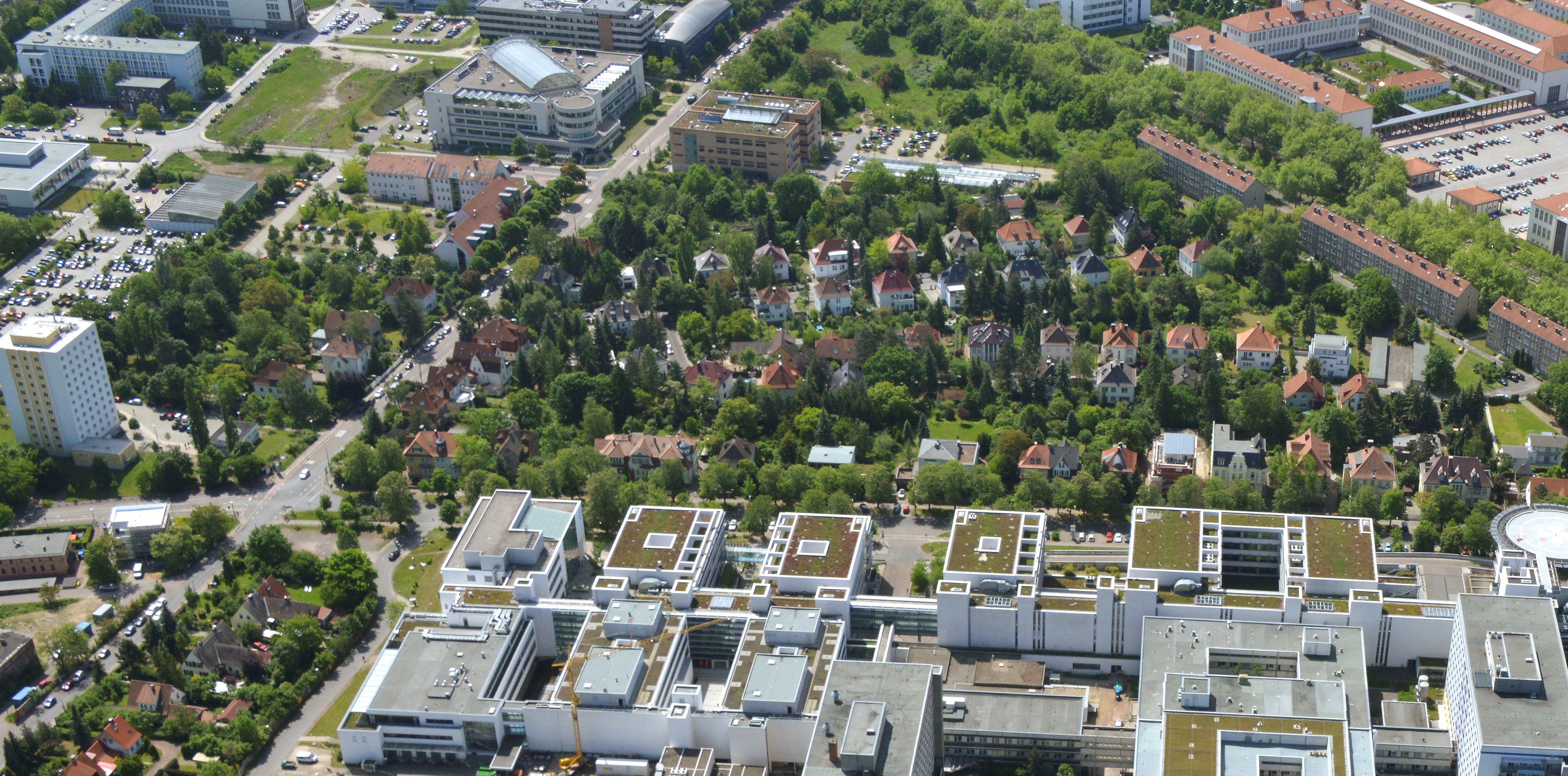 Luftbildaufnahme, auf der am unteren Bildrand das Universitätsklinikum liegt. Man blickt Richtung Weinberg Campus, links ist ein Studierendenwohnheim zu sehen sowie der Parkplatz und die Sporthalle. Weiter mittig das Wohngebiet mit viel Grün und in der oberen rechte Ecke ist der Heide-Campus angeschnitten.