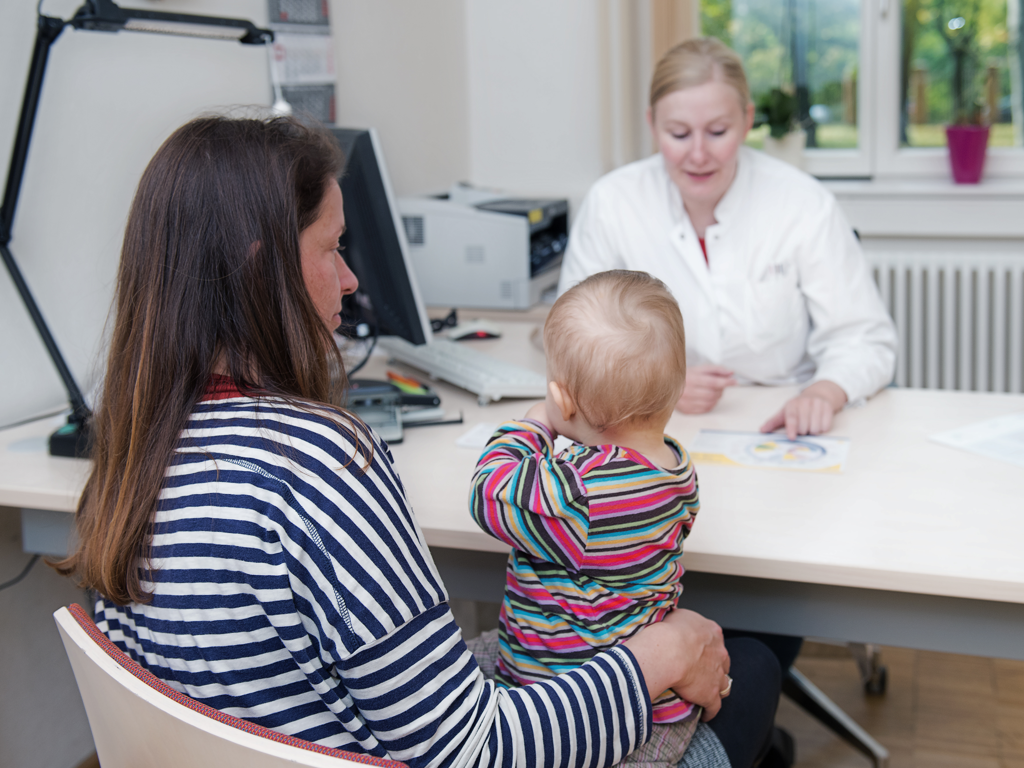 Mutter mit Kind auf dem Schoß im Gespräch mit einer Ärztin