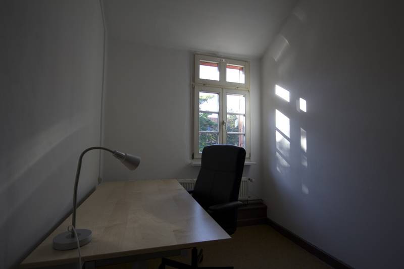 Kleines, dunkles Zimmer mit Schreibtisch, Stuhl und Lampe