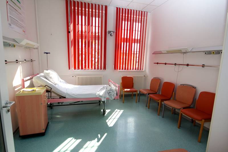 Leeres, voll eingerichtetes Krankenhauszimmer mit Bett, Nachttisch und Stühlen
