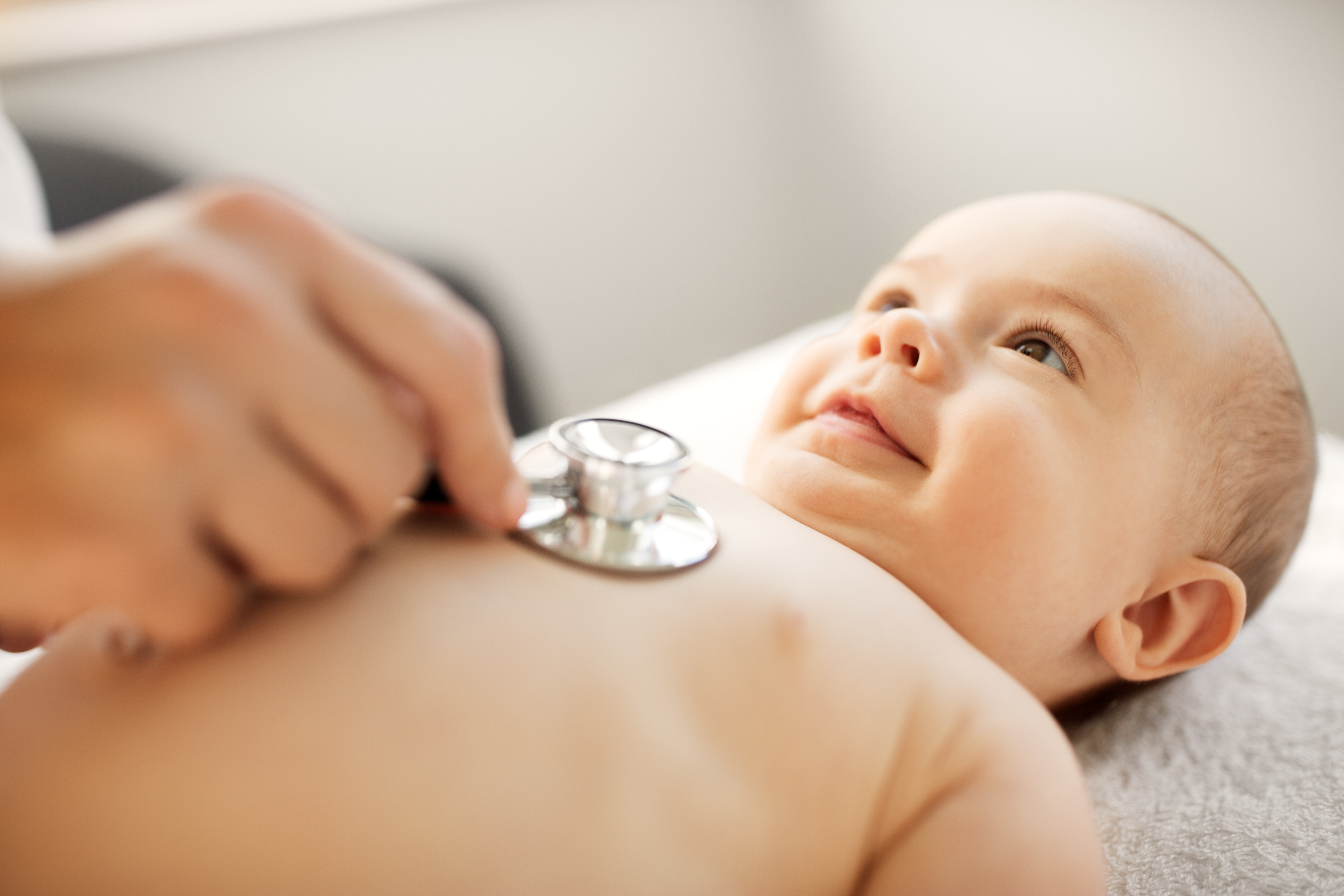 Baby liegt bei einer Untersuchung auf dem Rücken. Eine Hand hält ein Stetoskop auf den Brustkorb