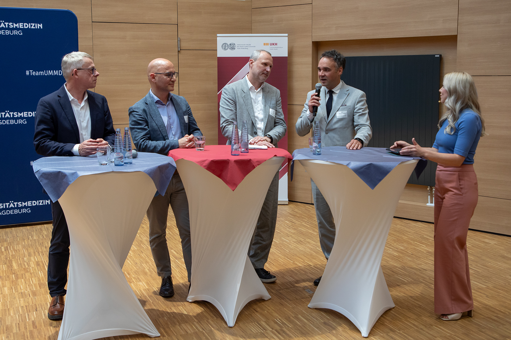 Vier Männer und eine Frau stehen an Stehtischen bei einem Paneltalk.