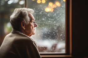 Ein älterer Mann sitzt an einem Fenster und schaut nach draußen.