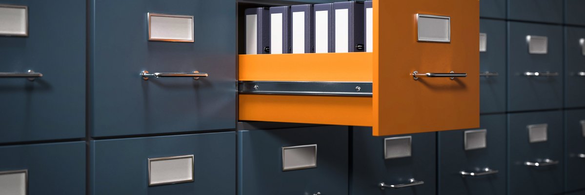 Aktenschrank mit grauen Fächern. Eine Schublade in orange ist geöffnet. Dort stehen Aktenordner