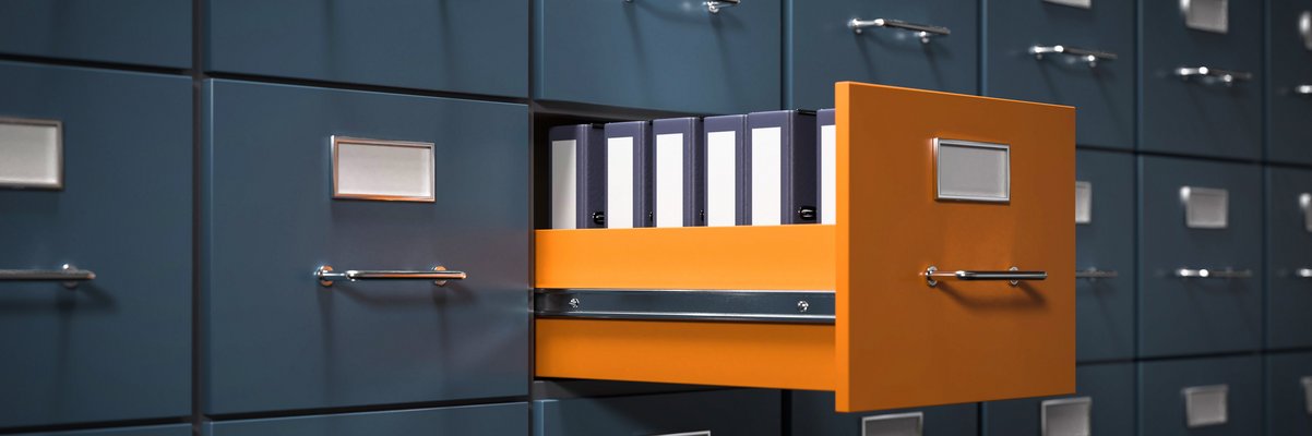 Aktenschrank mit grauen Fächern. Eine Schublade in orange ist geöffnet. Dort stehen Aktenordner