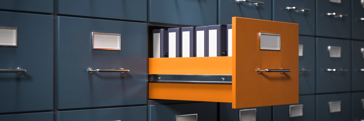 Aktenschrank mit grauen Fächern. Eine Schublade in orange ist geöffnet. Dort stehen Aktenordner