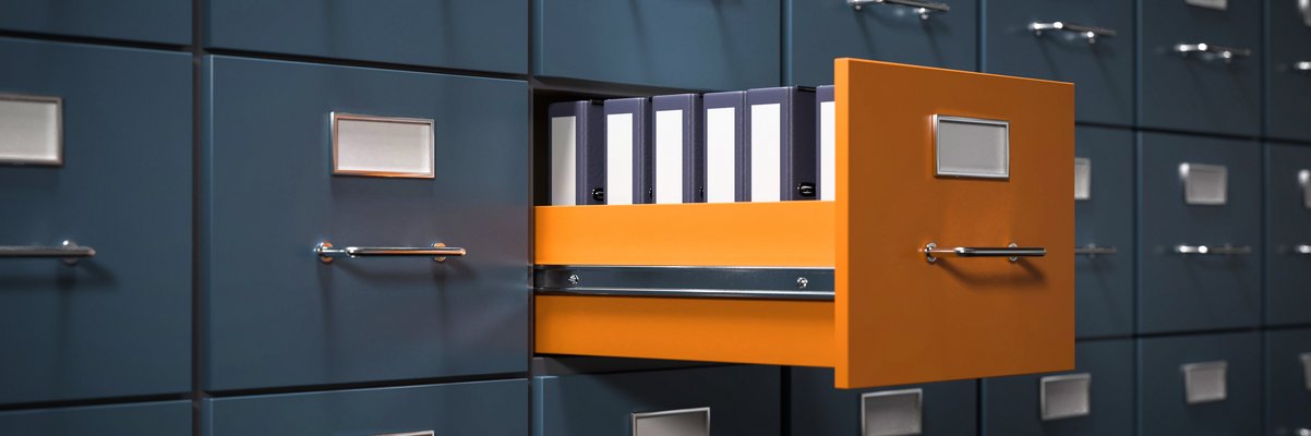 Aktenschrank mit grauen Fächern. Eine Schublade in orange ist geöffnet. Dort stehen Aktenordner