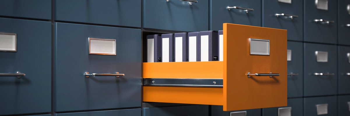 Aktenschrank mit grauen Fächern. Eine Schublade in orange ist geöffnet. Dort stehen Aktenordner