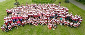 Eine große Menschenmenge in rot-weißen Shirts steht auf einer Wiese