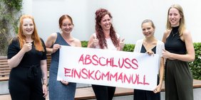 5 junge Frauen stehen nebeneinander und halten ein Banner. Aufschrift: abschluss einskommanull!