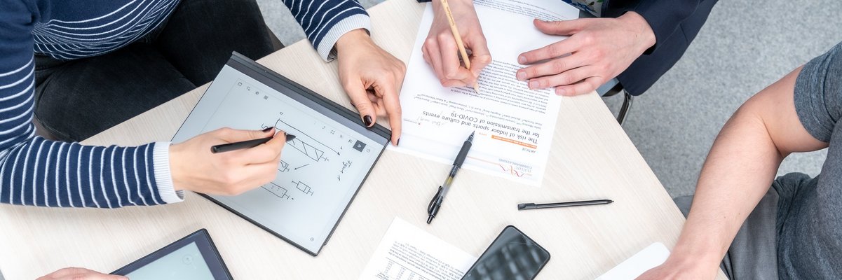 Menschen an einem Tisch mit Laptops, Schreibblock, Stiften