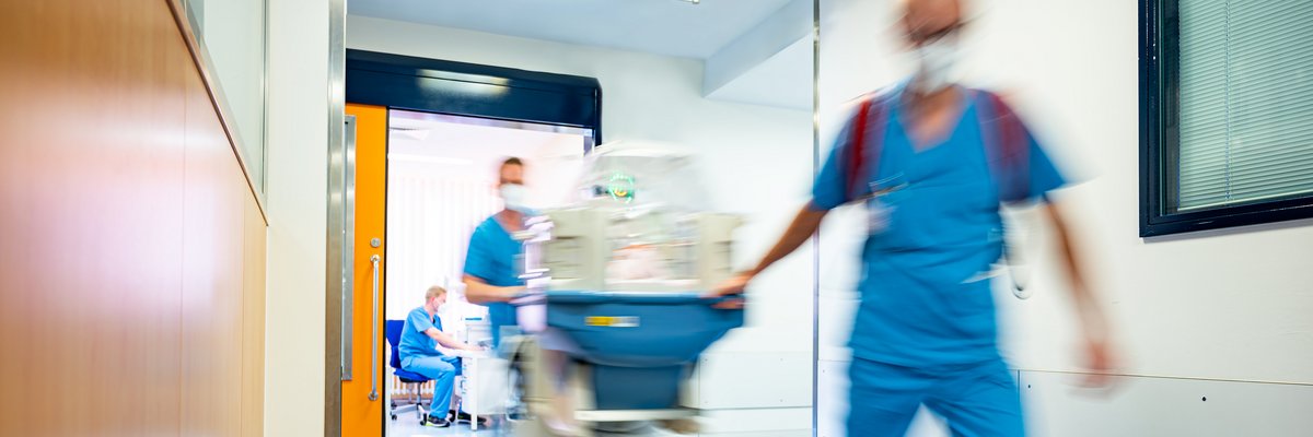 Medizinisches Personal zieht einen Inkubator schnell über den Gang