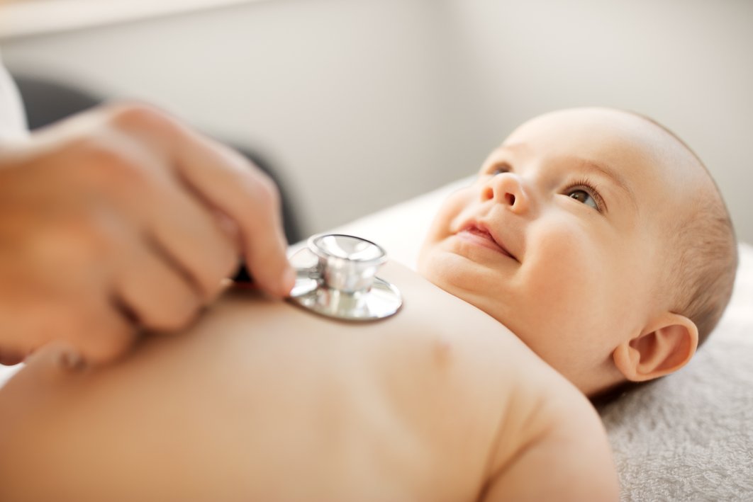 Baby liegt bei einer Untersuchung auf dem Rücken. Eine Hand hält ein Stetoskop auf den Brustkorb