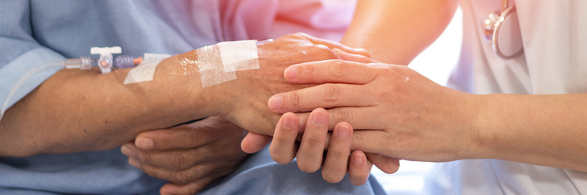 Frau mit Stetoskop hält die Hand mit gelegtem Zugang einer Patientin