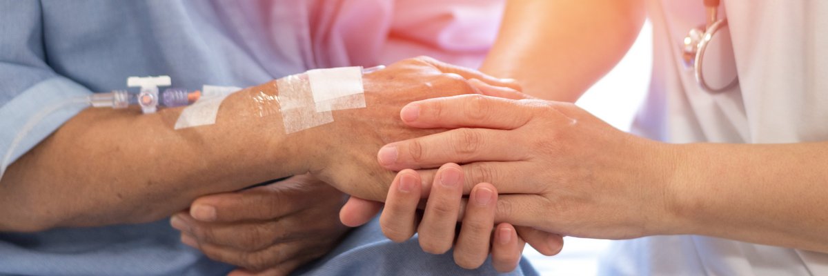 Frau mit Stetoskop hält die Hand mit gelegtem Zugang einer Patientin