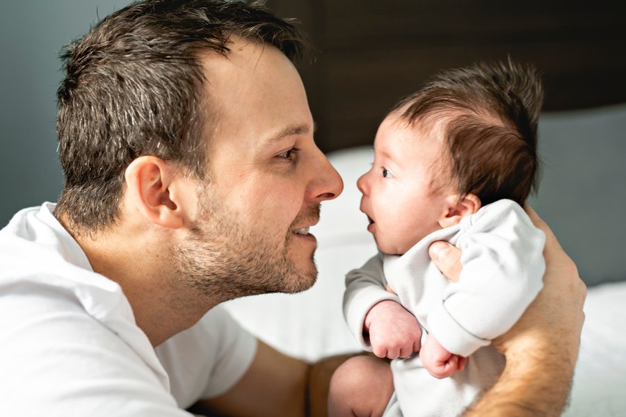 Ein junger Vater hält sein neugeborenes Baby fest. Sie schauen sich an, der Vater lächelt, das Baby hat die Augen weit geöffnet. Beide sind im Profil zu sehen, die Nasenspitzen berühren sich beinahe.  Ein junger Vater hält sein neugeborenes Baby fest. Sie schauen sich an, der Vater lächelt, das Baby hat die Augen weit geöffnet. Beide sind im Profil zu sehen, die Nasenspitzen berühren sich beinahe.