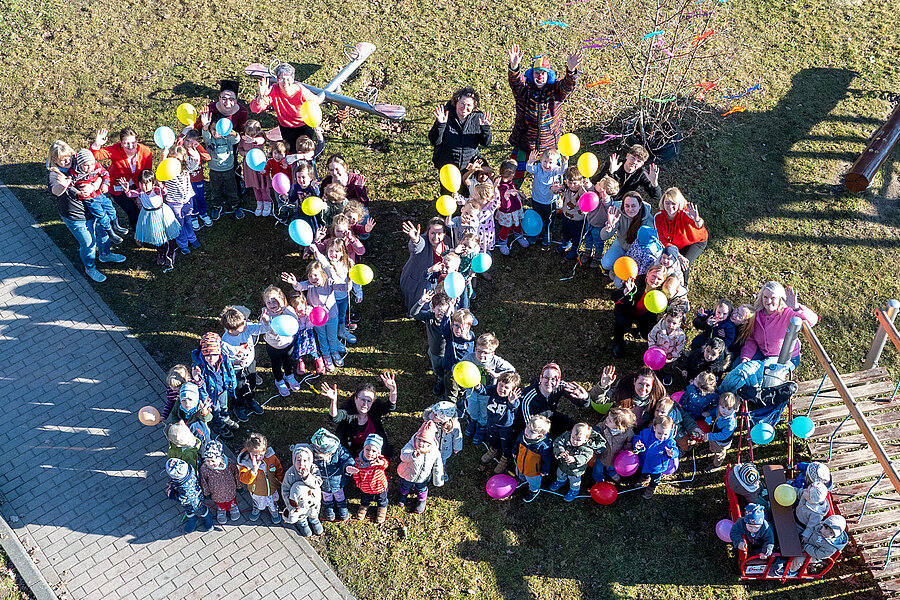 Aufnahme aus der Vogelperspektive. Eine Gruppe von Kindern und einigen Erwachsenen posiert in Form einer 20 auf einer Grünfläche.  Aufnahme aus der Vogelperspektive. Eine Gruppe von Kindern und einigen Erwachsenen posiert in Form einer 20 auf einer Grünfläche.