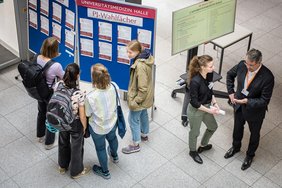 Eine Gruppe junger Menschen unterhält sich vor Infotafeln.