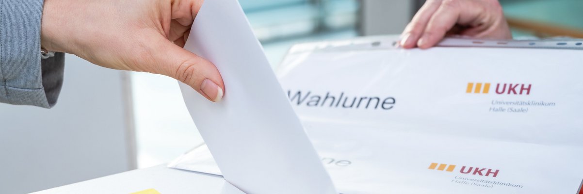 Wahlurne, in die gerade ein Wahlzettel gesteckt wird