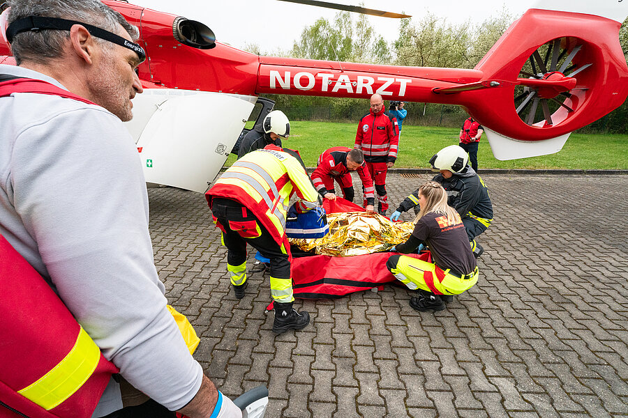 Rettungsteam versorgt verletzte Person neben einem Notarzthubschrauber auf einem Parkplatz.  Rettungsteam versorgt verletzte Person neben einem Notarzthubschrauber auf einem Parkplatz.