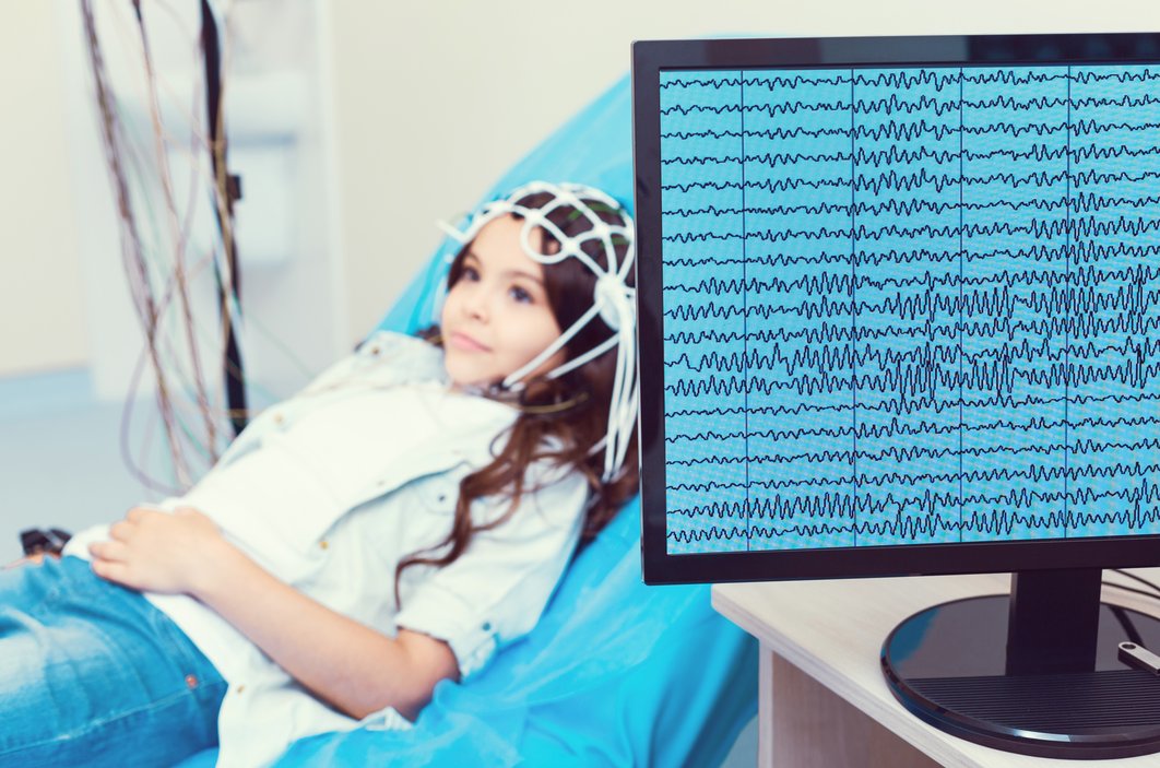 Mädchen liegt auf Liege und bekommt Hirnströme gemessen. EEG ist auf dem Monitor sichtbar