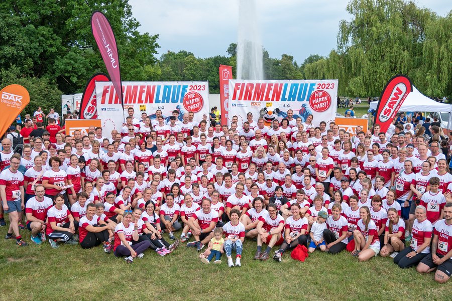 Gruppenfoto mit allen Mitarbeitenden der UMH, die am Firmenlauf 2023 in Halle teilgenommen haben. Im Hintergrund befinden sich Banner und Fahnen.  Gruppenfoto mit allen Mitarbeitenden der UMH, die am Firmenlauf 2023 in Halle teilgenommen haben. Im Hintergrund befinden sich Banner und Fahnen.