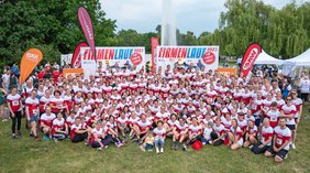 Gruppenfoto mit allen Mitarbeitenden der UMH, die am Firmenlauf 2023 in Halle teilgenommen haben. Im Hintergrund befinden sich Banner und Fahnen.