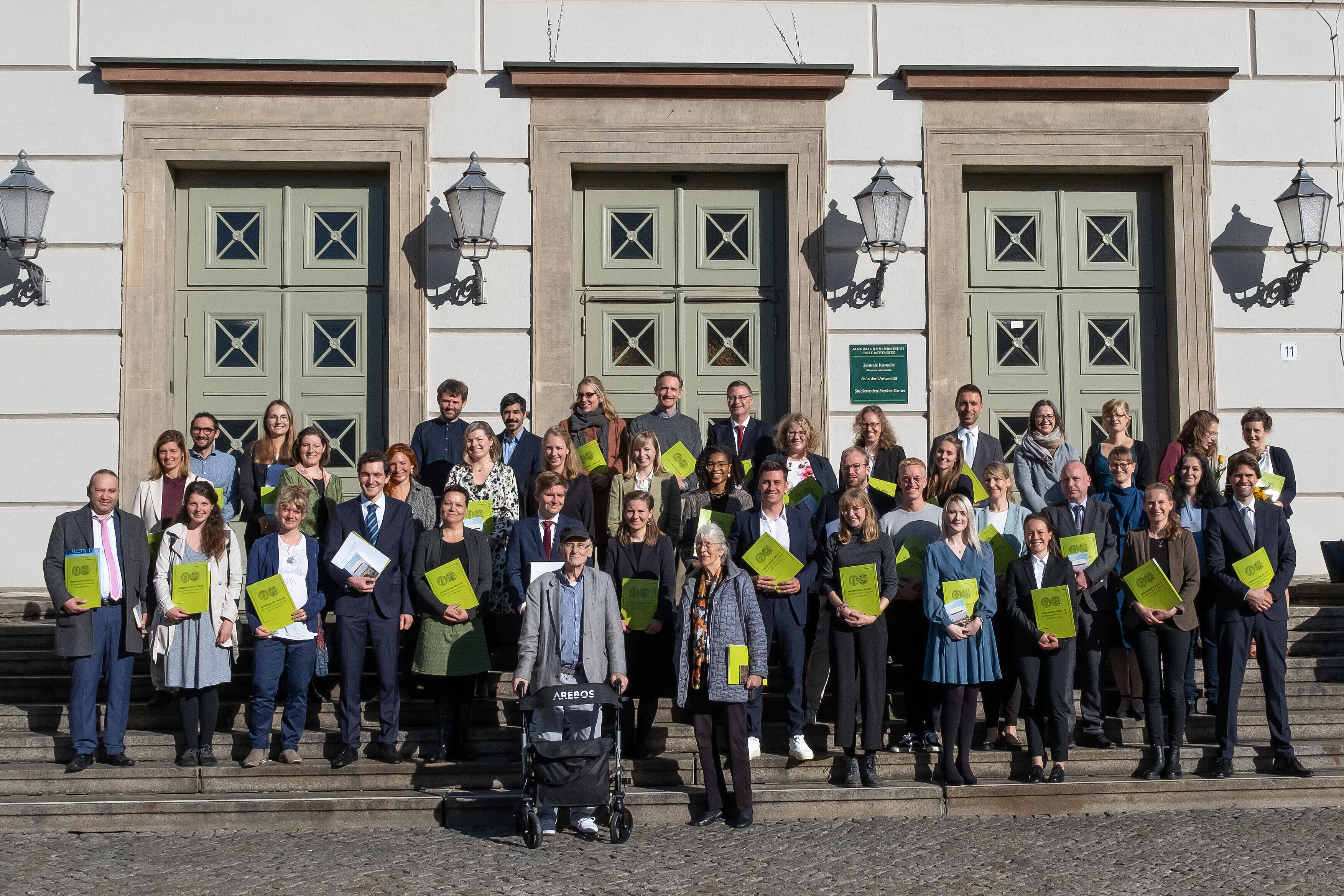 Eine Gruppe mit Urkunden steht auf den Treppen zum Löwengebäude am Uniplatz.