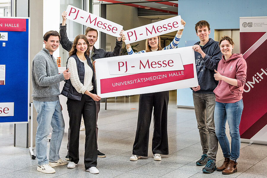 Sechs junge Menschen Sie halten Schilder mit der Aufschrift "PJ-Messe" und "Universitätsmedizin Halle" in die Höhe und zeigen "Daumen hoch".  Sechs junge Menschen Sie halten Schilder mit der Aufschrift "PJ-Messe" und "Universitätsmedizin Halle" in die Höhe und zeigen "Daumen hoch".