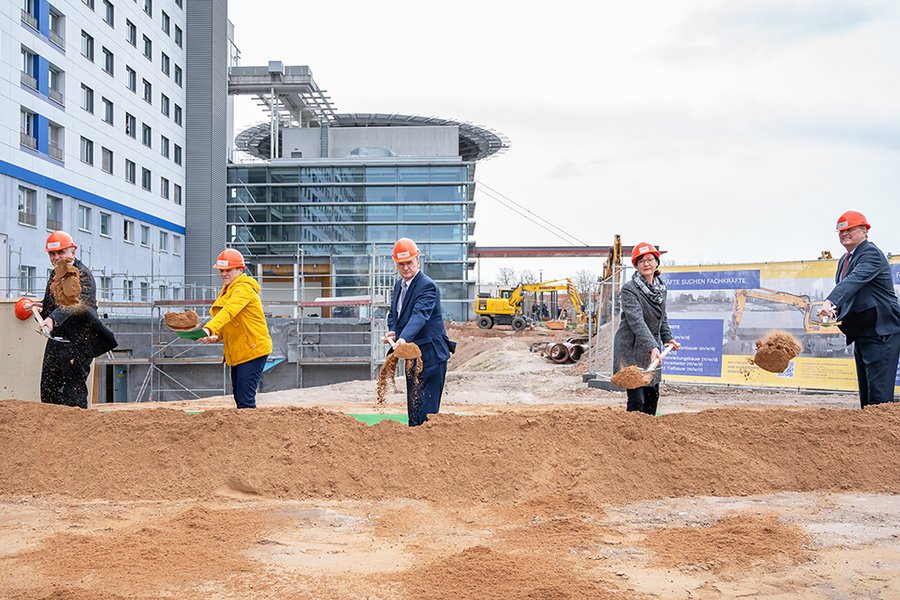 Fünf Menschen beim Spatenstich für neues Gebäude der Universitätsmedizin Halle (Saale). Im Hintergrund ist das Hauptgebäude des Universitätsklinikum zu sehen.  Fünf Menschen beim Spatenstich für neues Gebäude der Universitätsmedizin Halle (Saale). Im Hintergrund ist das Hauptgebäude des Universitätsklinikum zu sehen.