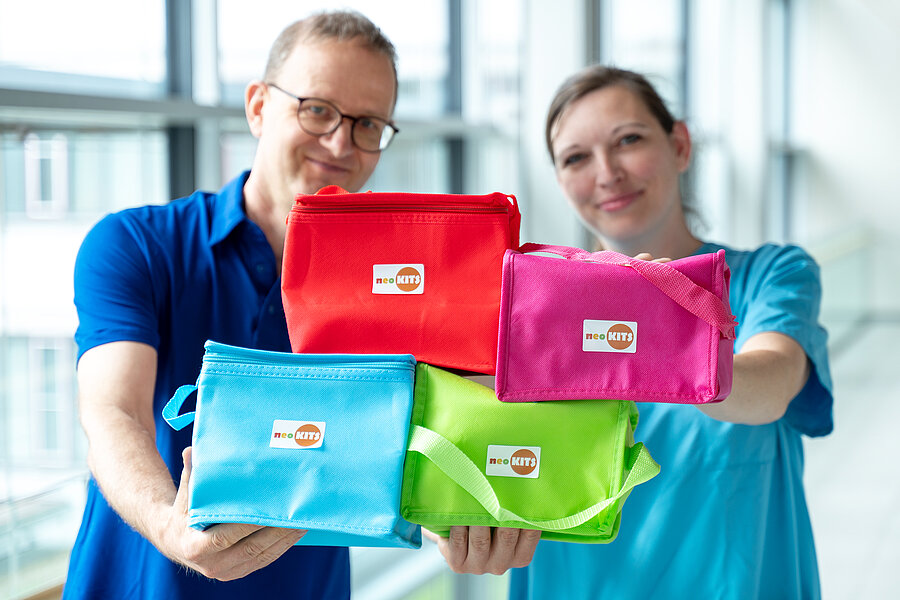 Zwei Personen halten vier Kühltaschen in die Kamera. Die Kühltaschen stehen im Fokus, die Personen sind unscharf.  Zwei Personen halten vier Kühltaschen in die Kamera. Die Kühltaschen stehen im Fokus, die Personen sind unscharf.