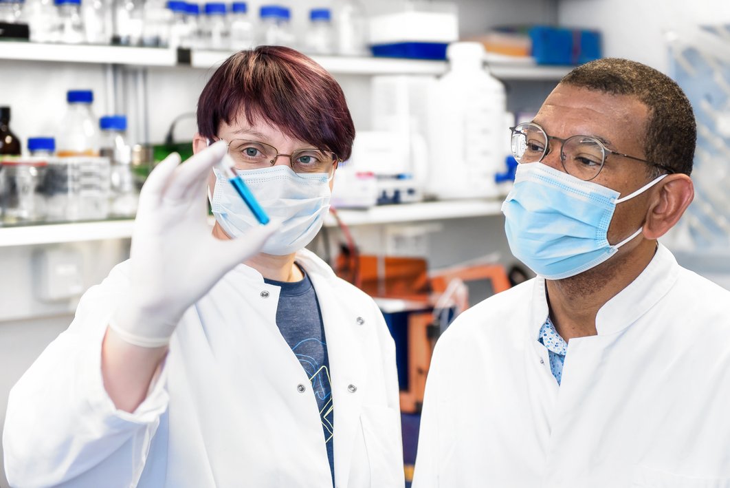 Ein Laborant und eine Laborantin schauen sich eine blaue Flüssigkeit in einem Reagenzglas an