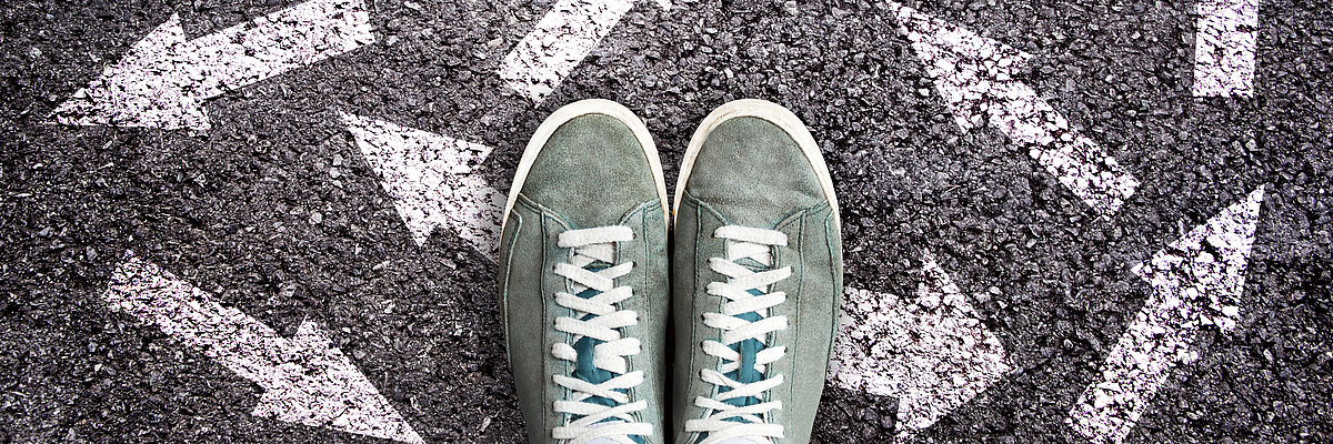 Turnschuhe stehen auf dem Asphalt mit vielen weißen Pfeilen in unterschiedlichste Richtungen