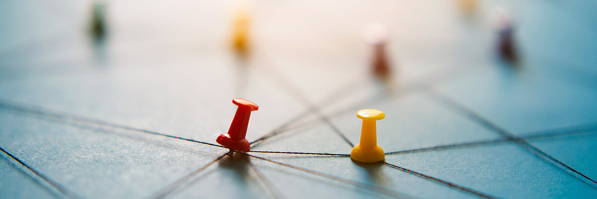 Gespannte Fäden auf einem Brett, an deren Schnittpunkten bunte Stecknadeln sitzen. Symbolhaft für Vernetzung