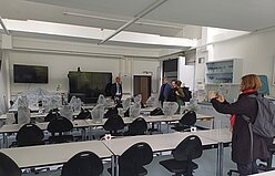 Mikroskopiersaal mit parallel angeordneten langen Tischreihen. An jedem Platz steht ein Mikroskop. Weil der Raum gerade nicht genutzt wird, sind diese mit transparenten Hüllen abgedeckt. Frontal befinden sich Bildschirme an bzw. vor der Wand. Rechts stehen Schränke mit Mikroskopiermaterial.