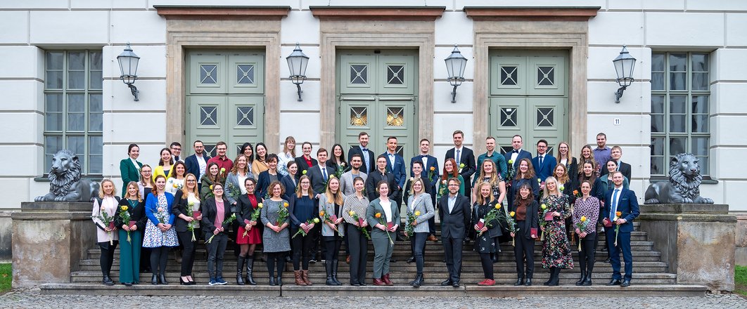 Eine Gruppe junger Menschen stehen auf der Treppe des Löwengebäudes auf dem Uniplatz.