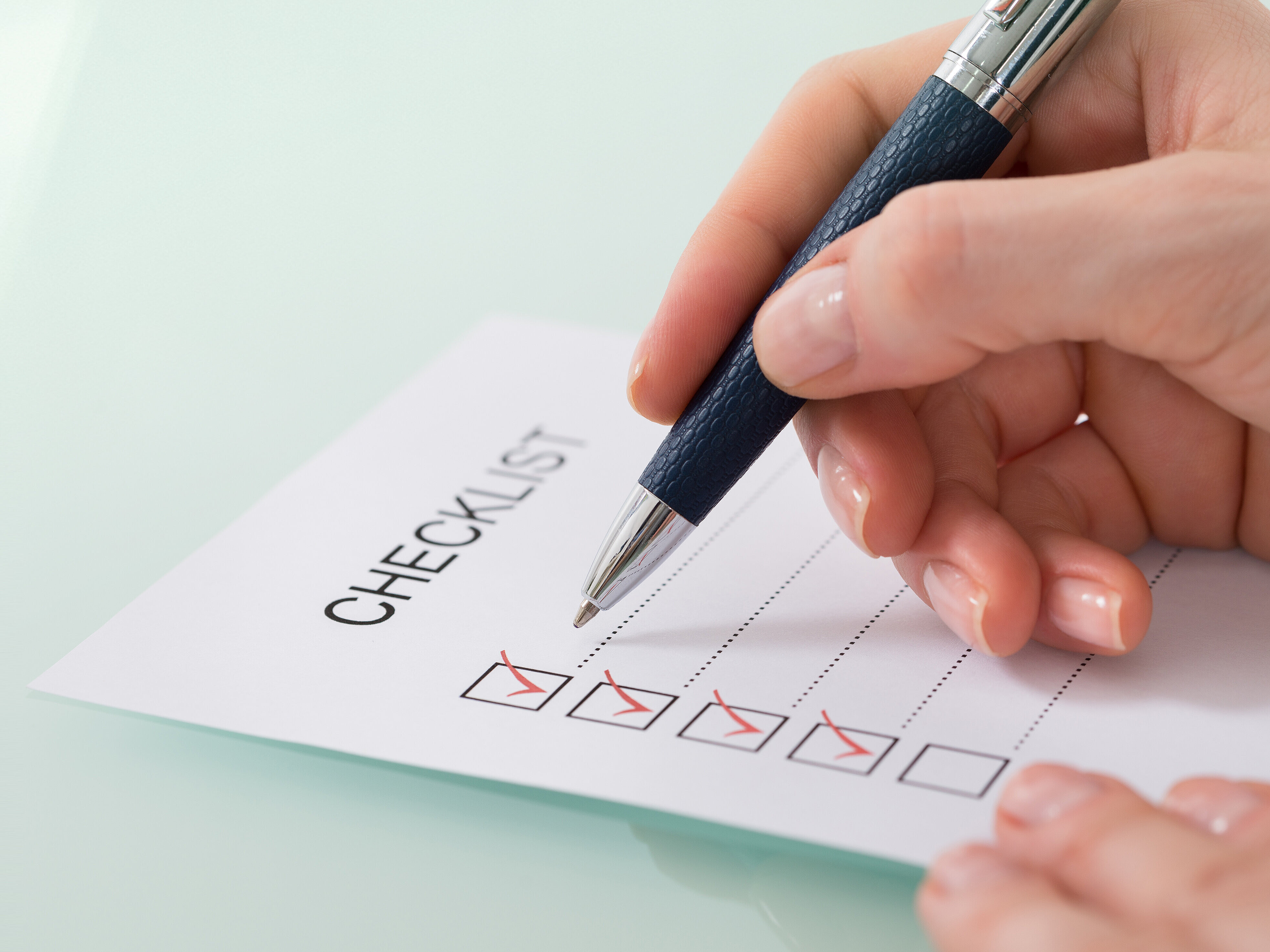 Hand mit Kugelschreiber streicht eine Checkliste ab