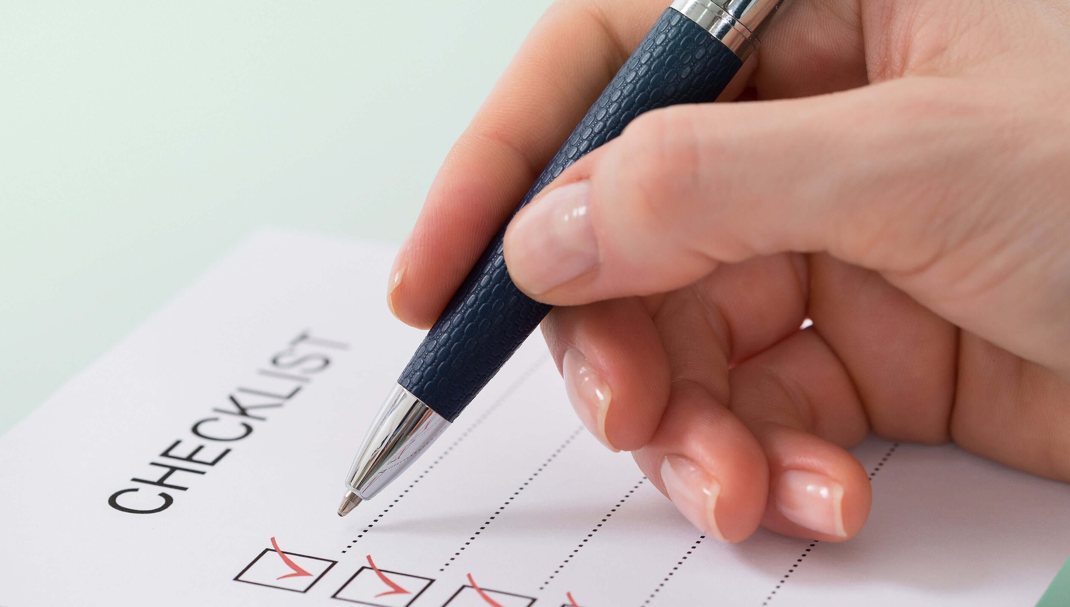 Hand mit Kugelschreiber streicht eine Checkliste ab