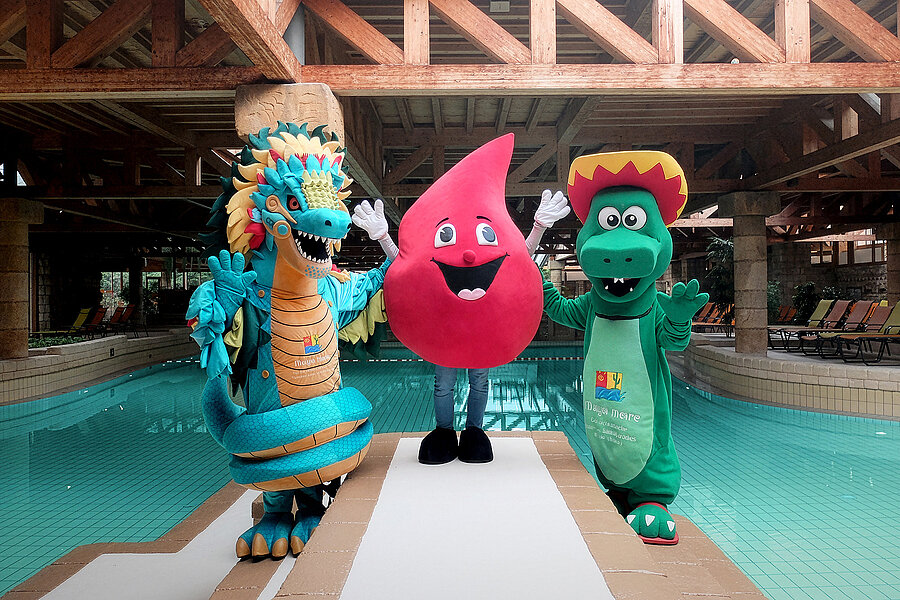 Die Maskottchen des Maya mare (links und rechts) und der Blutspende des Universitätsklinikums Halle (Saale) (Mitte) stehen zusammen am Beckenrand im Schwimmbad Maya mare. Die Maskottchen des Maya mare sind ein Drache und ein Krokodil, das Maskottchen des Klinikums ist ein großer Blutstropfen. Die Maskottchen des Maya mare (links und rechts) und der Blutspende des Universitätsklinikums Halle (Saale) (Mitte) stehen zusammen am Beckenrand im Schwimmbad Maya mare. Die Maskottchen des Maya mare sind ein Drache und ein Krokodil, das Maskottchen des Klinikums ist ein großer Blutstropfen.