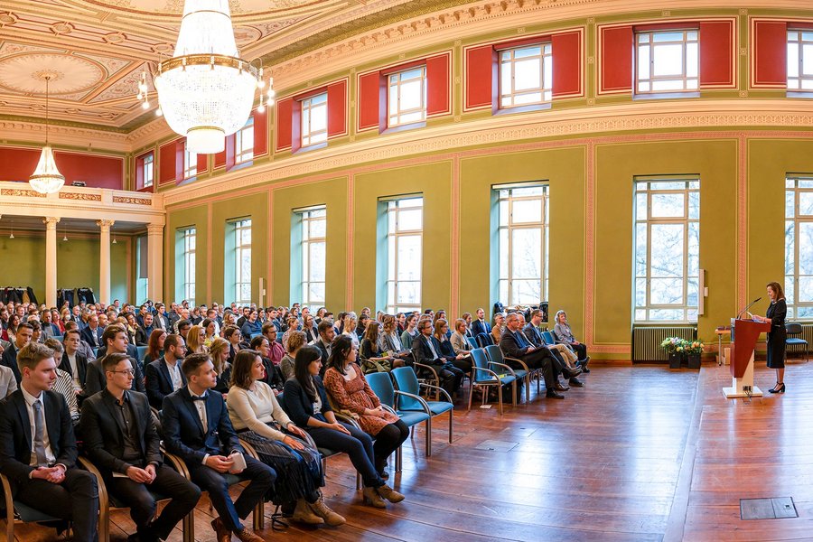 Mehrere Hundert Menschen in der Aula des Löwengebäudes, während eine Frau am Podium spricht.  Mehrere Hundert Menschen in der Aula des Löwengebäudes, während eine Frau am Podium spricht.