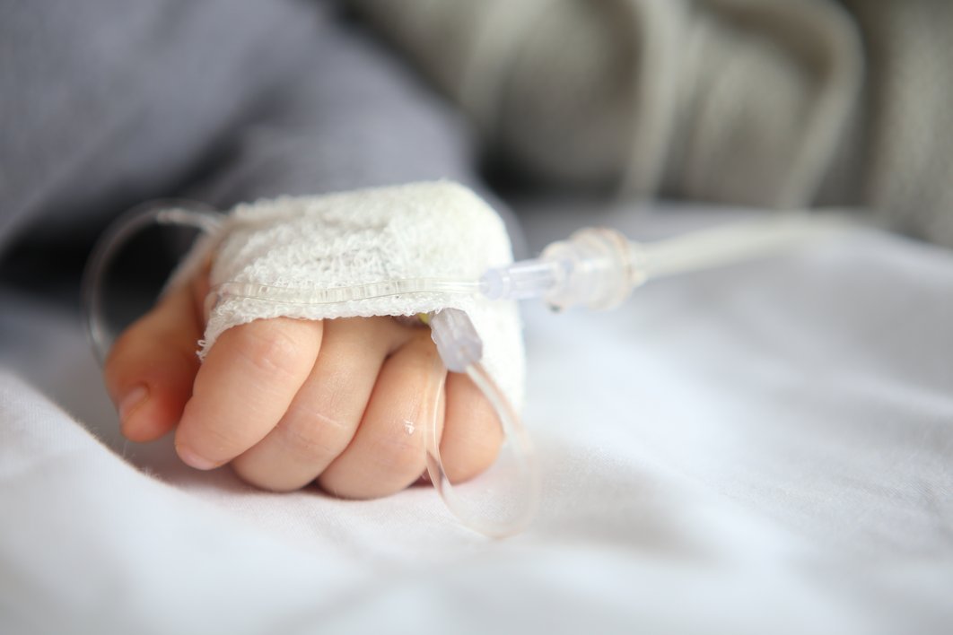 verbundene Kinderhand, die auf einem weißen Laken liegt und am Tropf angeschlossen ist