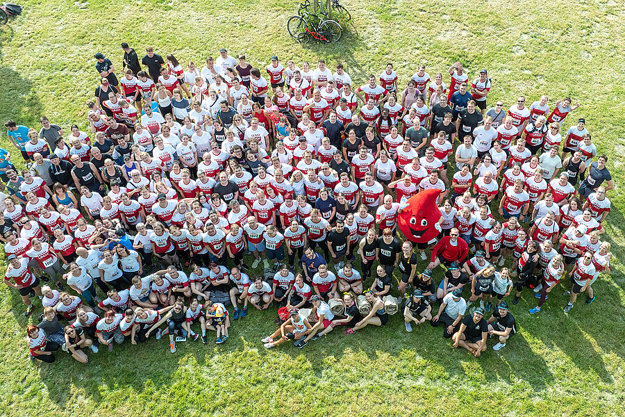 Eine große Menschenmenge in rot-weißen Shirts steht auf einer Wiese  Eine große Menschenmenge in rot-weißen Shirts steht auf einer Wiese