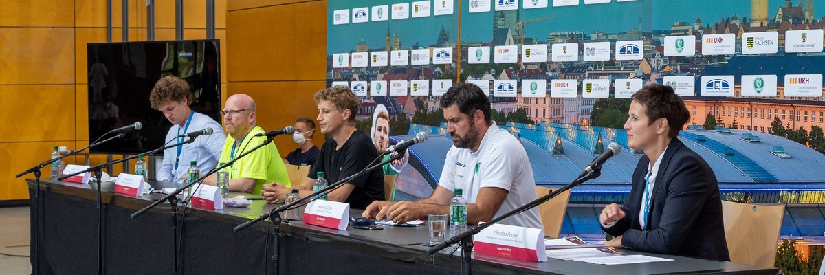 Menschen sitzen bei einer Pressekonferenz an einem langen Tisch mit Mikrofonen