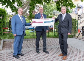 Symbolische Übergabe einer Nutzungsvereinbarung für ein Gartenstück zum 30-jährigen Jubiläum des "Kinderplaneten" der Kinderkrebshilfe Halle: Ministerpräsident Dr. Reiner Haseloff (links), der Ärztliche Direktor Prof. Dr. Thomas Moesta (Mitte) und Vereins-Vorstands-Vorsitzender Andreas Domaske (rechts) halten jeweils mit einer Hand das große Dokument fest.