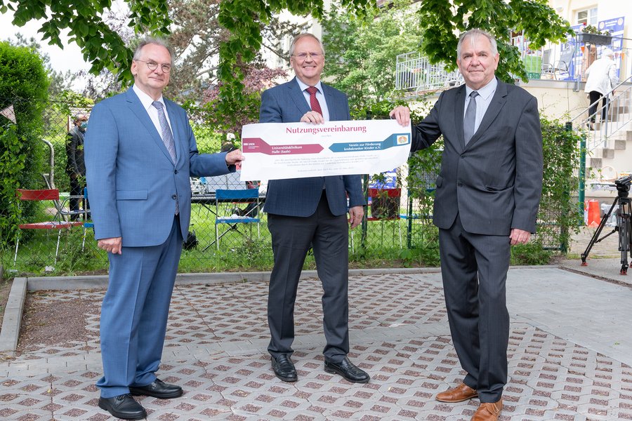 Symbolische Übergabe einer Nutzungsvereinbarung für ein Gartenstück zum 30-jährigen Jubiläum des "Kinderplaneten" der Kinderkrebshilfe Halle: Ministerpräsident Dr. Reiner Haseloff (links), der Ärztliche Direktor Prof. Dr. Thomas Moesta (Mitte) und Vereins-Vorstands-Vorsitzender Andreas Domaske (rechts) halten jeweils mit einer Hand das große Dokument fest.  Symbolische Übergabe einer Nutzungsvereinbarung für ein Gartenstück zum 30-jährigen Jubiläum des "Kinderplaneten" der Kinderkrebshilfe Halle: Ministerpräsident Dr. Reiner Haseloff (links), der Ärztliche Direktor Prof. Dr. Thomas Moesta (Mitte) und Vereins-Vorstands-Vorsitzender Andreas Domaske (rechts) halten jeweils mit einer Hand das große Dokument fest.