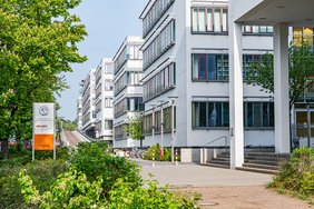 Außenansicht eines Klinikkomplexes. Am linken Bildrand sind grüne Büsche und Bäume sowie ein Schild mit der Aufschrift „Landeszentrum für Zell- und Gentherapie“ zu erkennen. In der rechten Bildhälfte staffeln sich mehrere modern anmutende Gebäudeteile, in denen sich Forschungs- und Behandlungsräume befinden.
