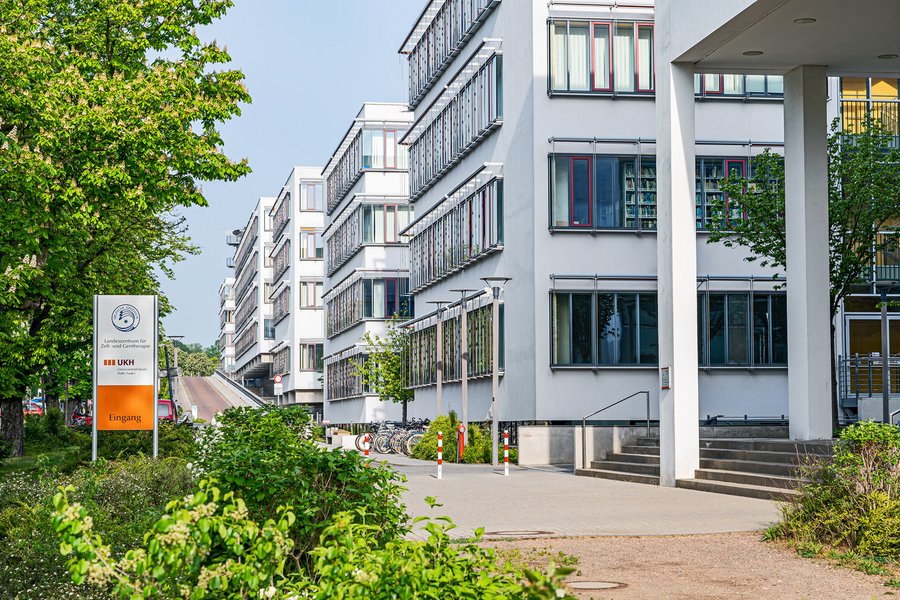 Außenansicht eines Klinikkomplexes. Am linken Bildrand sind grüne Büsche und Bäume sowie ein Schild mit der Aufschrift „Landeszentrum für Zell- und Gentherapie“ zu erkennen. In der rechten Bildhälfte staffeln sich mehrere modern anmutende Gebäudeteile, in denen sich Forschungs- und Behandlungsräume befinden.  Außenansicht eines Klinikkomplexes. Am linken Bildrand sind grüne Büsche und Bäume sowie ein Schild mit der Aufschrift „Landeszentrum für Zell- und Gentherapie“ zu erkennen. In der rechten Bildhälfte staffeln sich mehrere modern anmutende Gebäudeteile, in denen sich Forschungs- und Behandlungsräume befinden.
