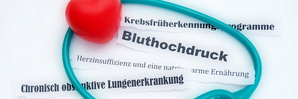 Türkisfarbendes Stetoskop mit rotem Herz auf den Worten Bluthochdruck und weiteren chronischen Krankheiten