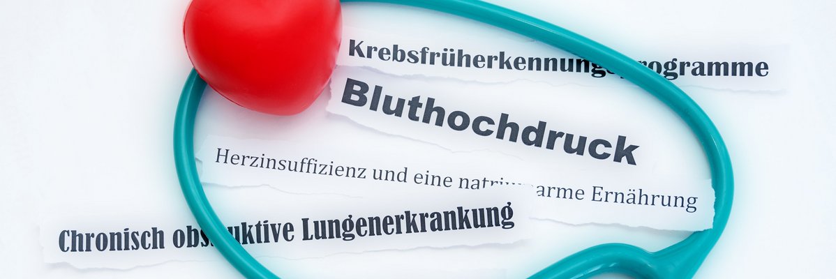 Türkisfarbendes Stetoskop mit rotem Herz auf den Worten Bluthochdruck und weiteren chronischen Krankheiten