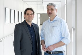 Dr. Tobias Esser und Prof. Dr. Martin Kaiser (v. l.) stehen in einem Gang im Hauptgebäude des Universitätsklinikums Halle (Saale).